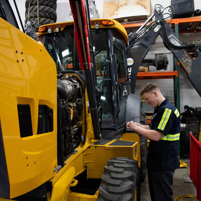 A student performs maintenance on a backhoe.
