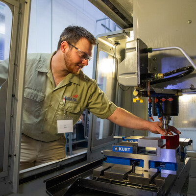 A student removes a piece of metal recently shaped inside a CNC milling machine.