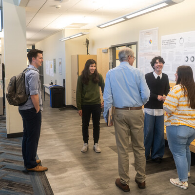 Students laugh with a member of the CWI faculty while presenting a poster that displays information from a research project.