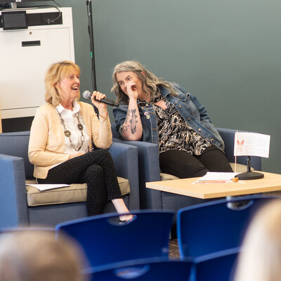 Two writing students laugh as they participate in a panel discussion in front of an audience.