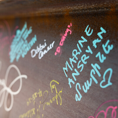 Signatures in teal, pink, white, and yellow are seen on a brown metal beam.