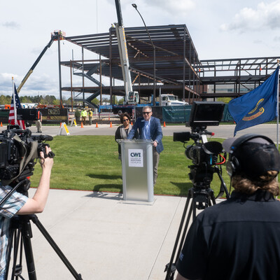 A CWI administrator speaks from a podium to news cameras in front of a construction site.