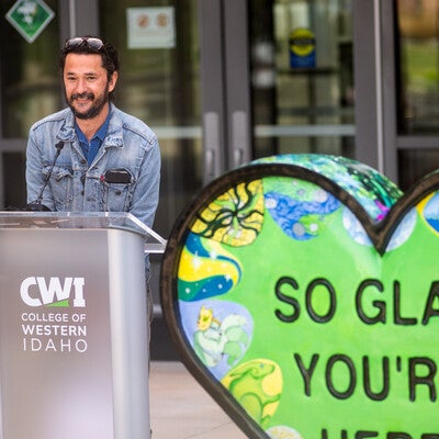 People attend the unveiling of a new artwork sculpture outside an academic building on a college campus.