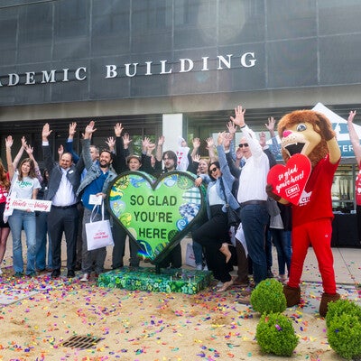 People attend the unveiling of a new artwork sculpture outside an academic building on a college campus.