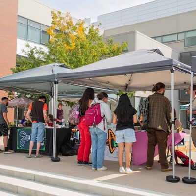 Students gather around two tables and two tents