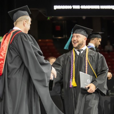 Graduate shaking hands with President Gordon Jones on stage during commencement
