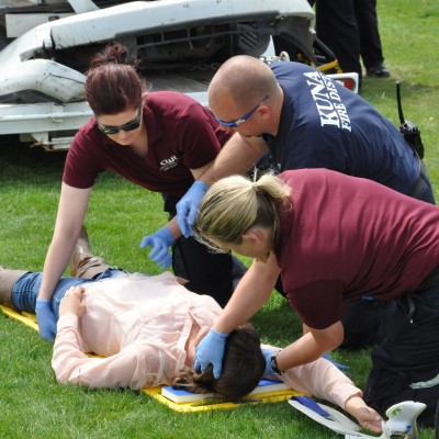 Advanced EMT students demonstrating CPR on lady laying on the ground.