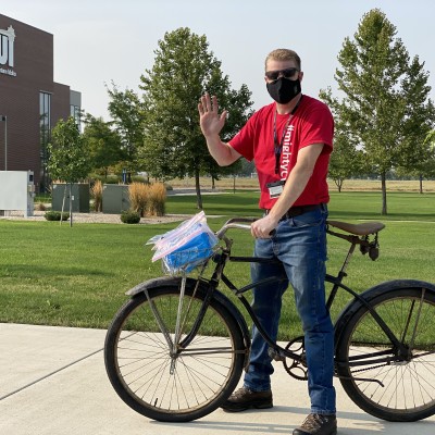 CWI staff member, Ross Hosking, handing out Be Safe, Be Mighty kits to students at the Nampa Campus Academic Building on a bike