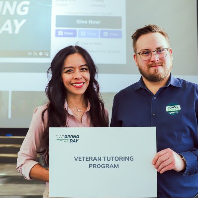 2 smiling people pose for a photo holding a white sign that says "Veteran Tutoring Program."