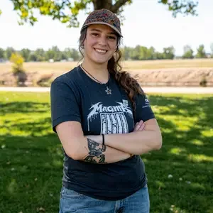 Person stands in front of tree and grass with arms crossed