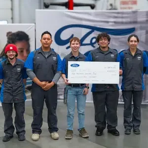 Five students stand together holding a large check