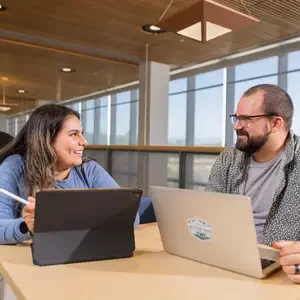 Two people using computers and devices at a table