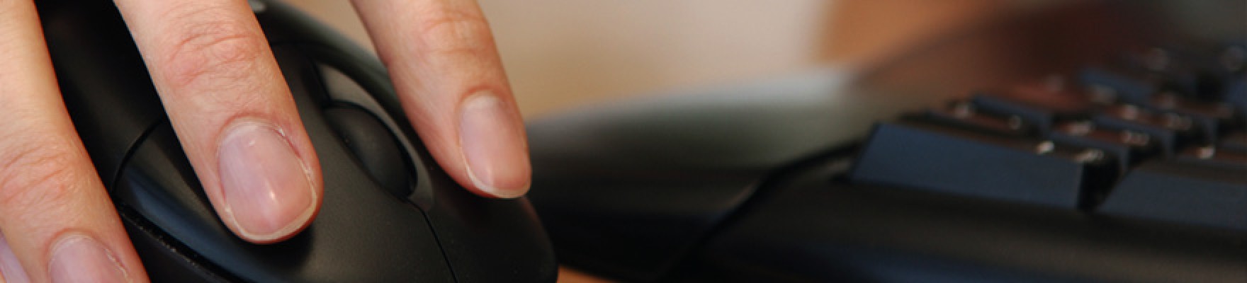 Close up of fingers on a computer mouse with keyboard in background.