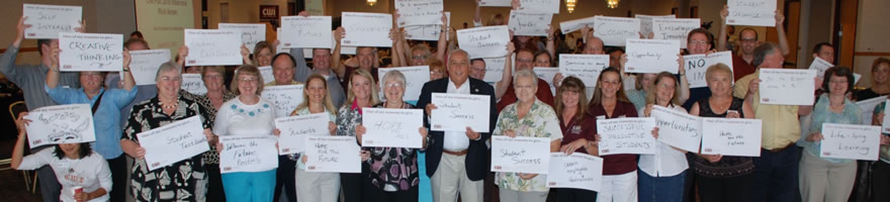 Large group of CWI employees with signs saying why they donate to scholarships.