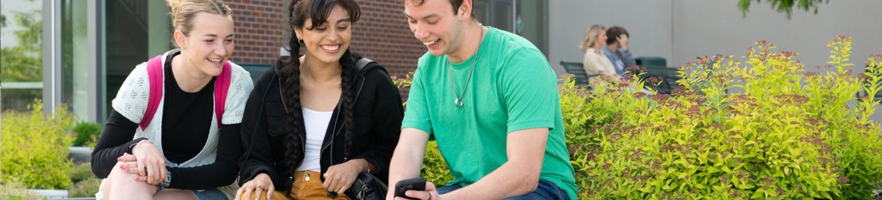 Students outside a campus building looking at a mobile phone