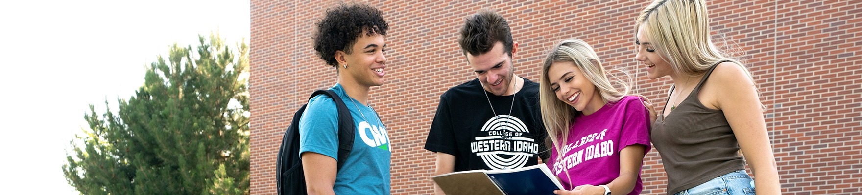 Group of students outside a campus building looking at a notebook together