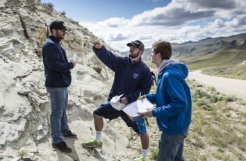 Three students on a rocky hill studying the rocks.