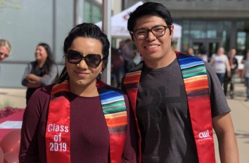 Latinx woman and man pose for picture with Latinx Stoles. 