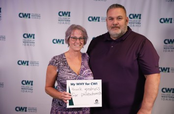Two people holding My Why for CWI signs with CWI backdrop