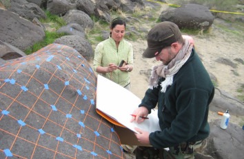 Two anthropology students studying rock paintings on boulder.