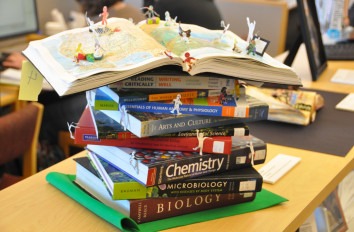 Tower of text books with paper people on open book at the top.