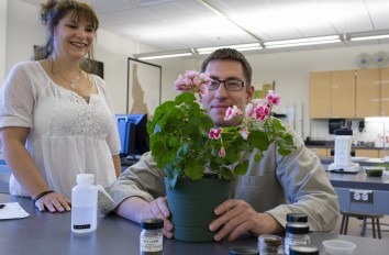 Female and male students at table with plant and jars of seeds.
