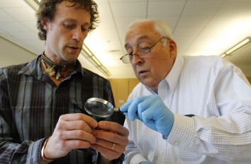 Dusty Perkins and Bert Glandon looking through magnify glass.