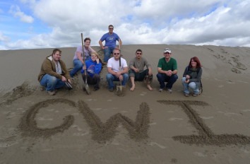Geology students sitting on a sand dune with CWI written in the sand.