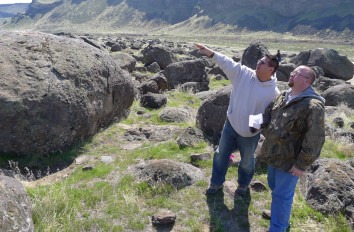 Two male Geology students in a field with large boulders.