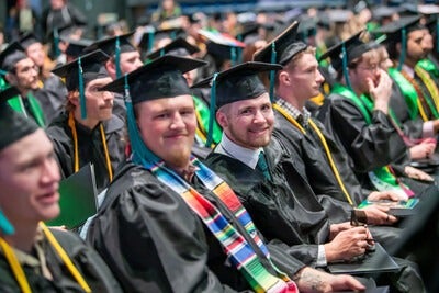 students smiling at camera in arena during commencement ceremony