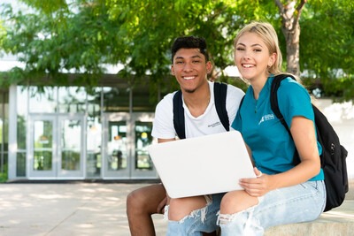 Students outside a campus building with a laptop