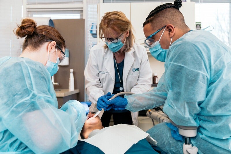 Dental Assisting students working on patient's teeth with instructor