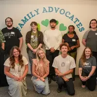 Group of 11 people stand and kneel in front of sign that says Family Advocates