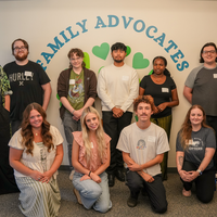 Group of 11 people stand and kneel in front of sign that says Family Advocates