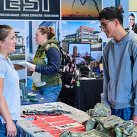 Employer speaking with student in front of table and gear