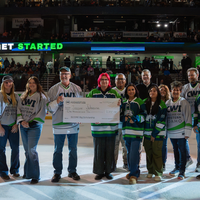 Group of people standing on ice holding large check in front of crowd