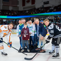 Group of people perform the puck with two hockey players off to the sides