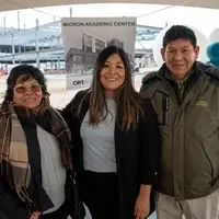 Three people standing in front of sign and balloons