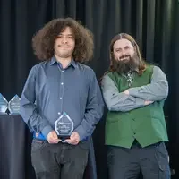 Two people stand side by side with an award