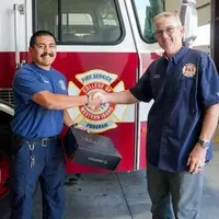 Two people shake hands in front of a fire truck 