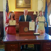 Three people stand behind podium holding a proclamation and certificates
