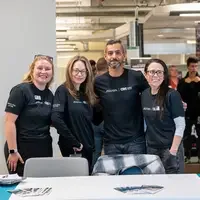 Four people stand together behind table