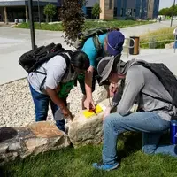 Three people working together around a rock