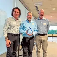 Three people standing together, with one person holding an award
