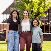 A mother and her two children stand smiling for a portrait in front of a construction site.