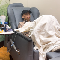 A woman sits in a chair undergoing chemotherapy.