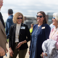 A group of 4 smiling people, dressed formally, laugh at an outdoor event.