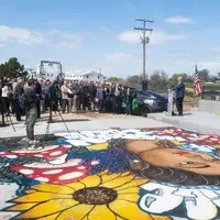 A large group of people listen to a man addressing the crowd, standing in front of a newly constructed bridge.
