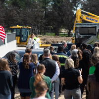 The chairwoman of the Board of Trustees addresses a crowd at an outdoor bridge dedication event.