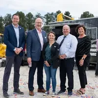 Four people smile as they look into the camera for a portrait in front of construction equipment on a newly build bridge.